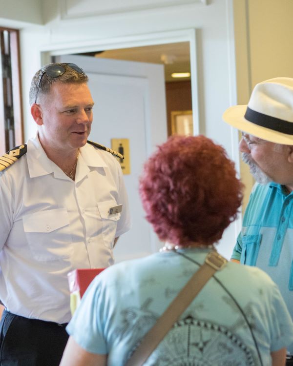 An Azamara crew member greets two guests onboard the ship