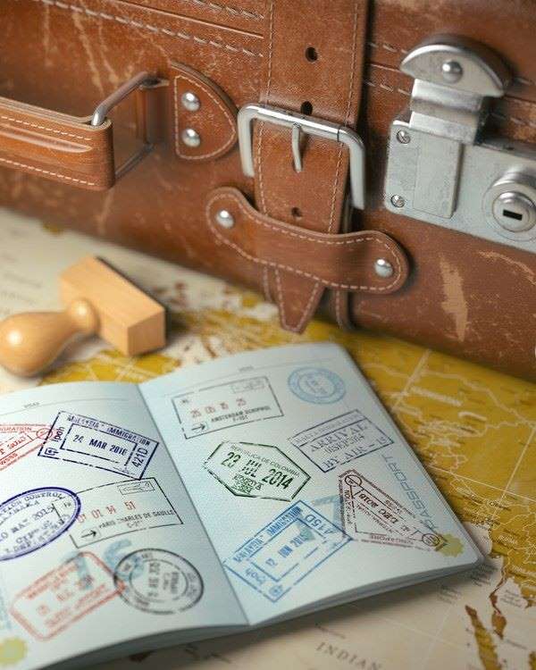 A passport, with many country stamps, lays open on a table with a suitcase