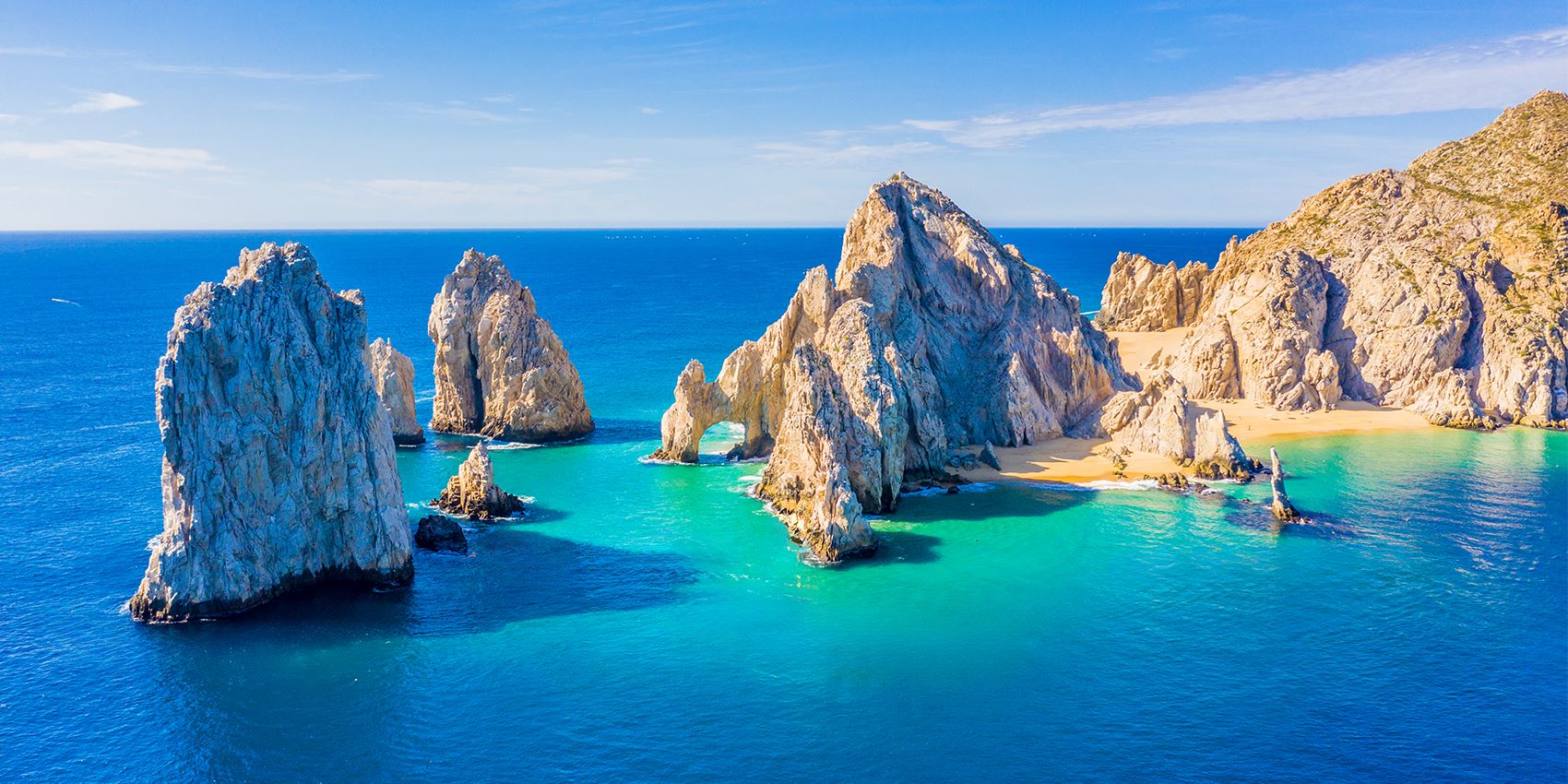 sunny sandy beach blue waters rocks jutting out of water