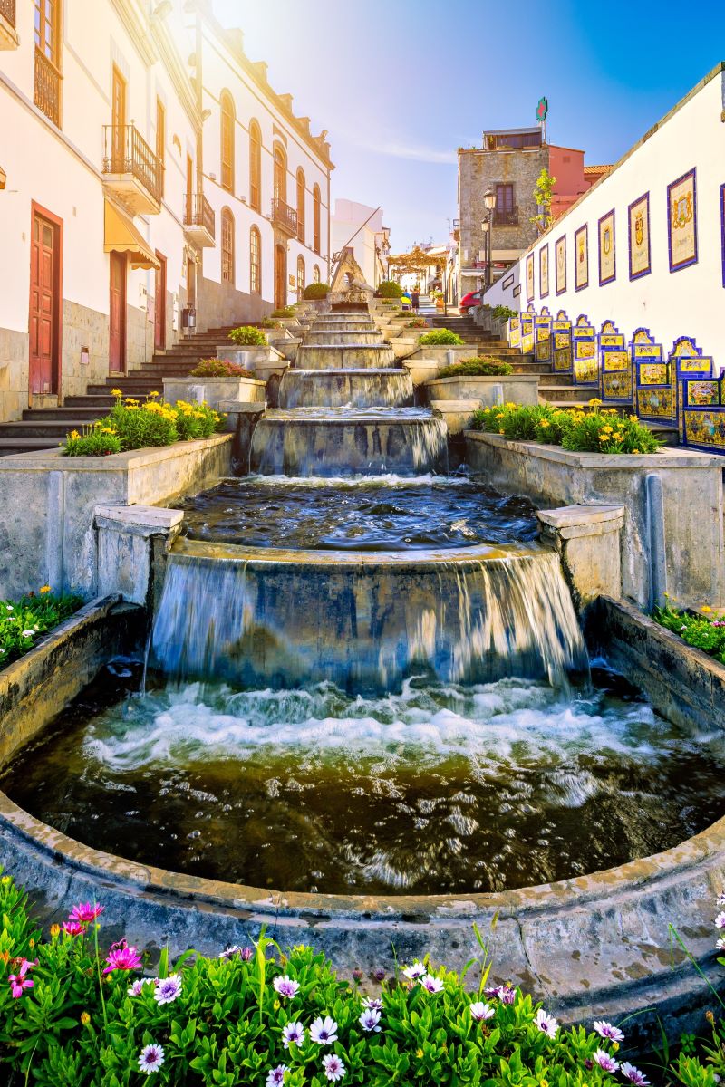 water fountain flowing down with plants and stairs on either side between buildings