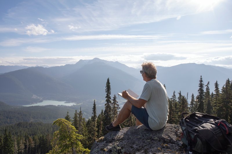 Male hiker relaxes on rock overlook, above valley